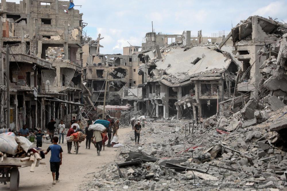  10月12日，在加沙地带南部汗尤尼斯，重返家园的巴勒斯坦人走过严重受损的建筑。新华社发（里泽克·阿卜杜勒贾瓦德摄）