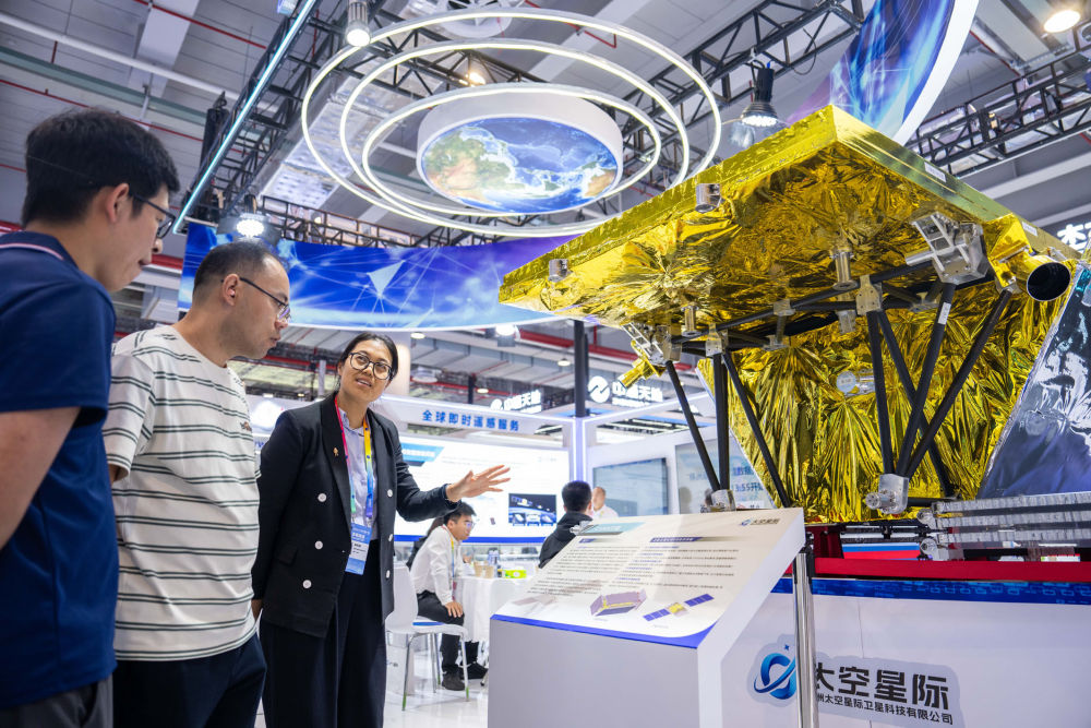 在湖南株洲国际会展中心举办的第四届北斗规模应用国际峰会上，工作人员（左三）在介绍一台对地观测卫星。新华社记者 陈思汗 摄